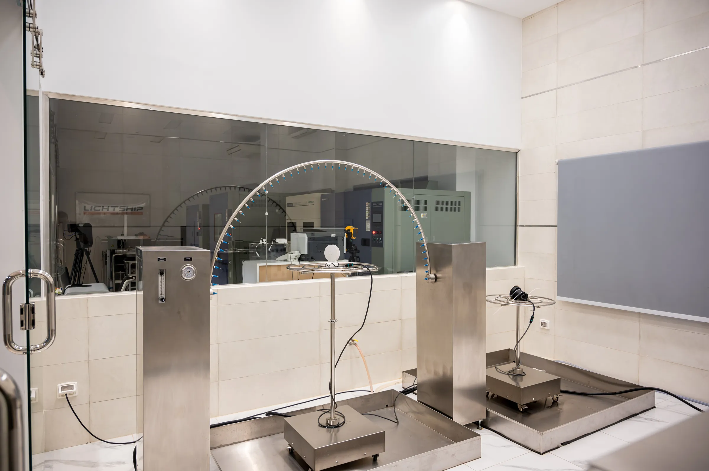 The same laboratory, photographed: the goniophotometer arc over a luminaire on its mount, with a second test station and the instrument room behind the glazing.